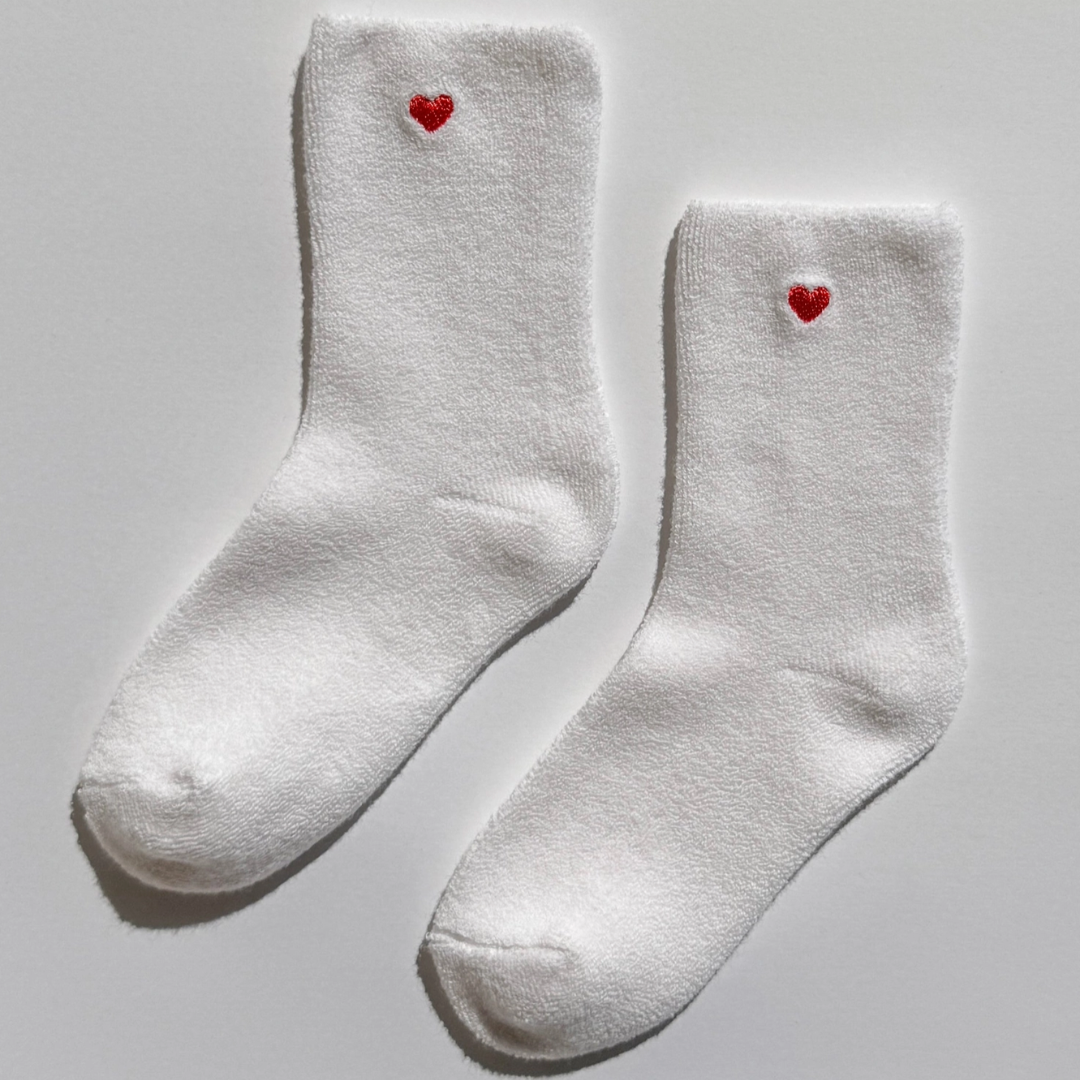 Pair of white socks with red embroidered heart on a white background.