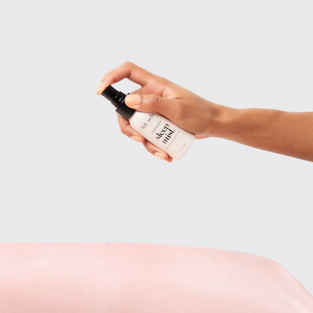 Hand holding a spray bottle labeled 'NATRUE' against a light gray background.