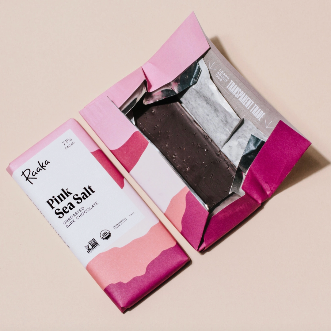 Pink and white packaging of a chocolate bar with visible Raaka brand name on a beige background.
