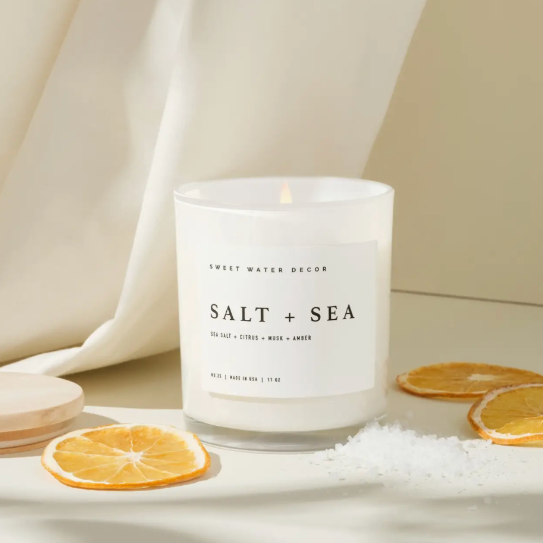 White glass candle labeled 'Salt + Sea' with decorative elements on a neutral background.