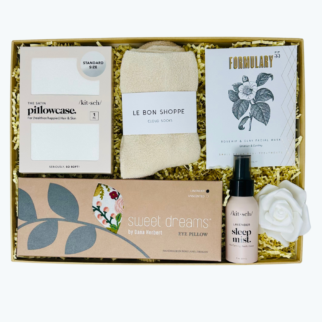 Gift set with satin pillowcase, eye pillow, cozy socks, facial mask, and sleep mist in a box.
