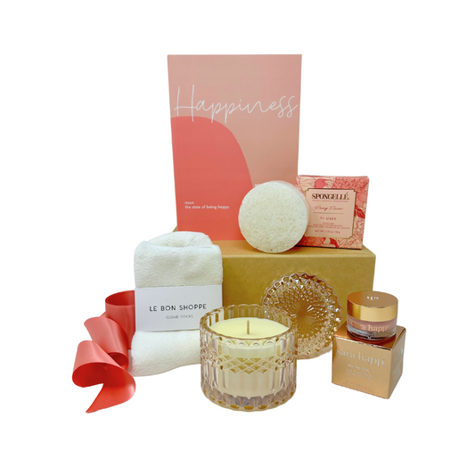 A curated "Send Happiness" gift box featuring five thoughtfully selected items for relaxation and self-care. Included is the Happiness Guided Journal, a Petite Shimmer Candle in Rose Vanilla scent housed in a diamond-cut glass vessel, a Peony Flower Infused Body Buffer from Spongellé, a Sara Happ Lip Slip® Balm for deeply hydrated lips, and Le Bon Shoppe Cozy Socks made from soft, breathable cotton. Perfect for spreading positivity and comfort to a loved one or treating yourself.