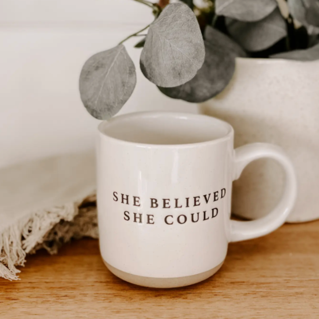 Close-up of a stoneware mug with a modern speckled design and the inspiring message "She Believed She Could" in classic black print. The cream-colored mug, with its hand-crafted details and natural base, is perfect for daily use and is safe for microwave and dishwasher.