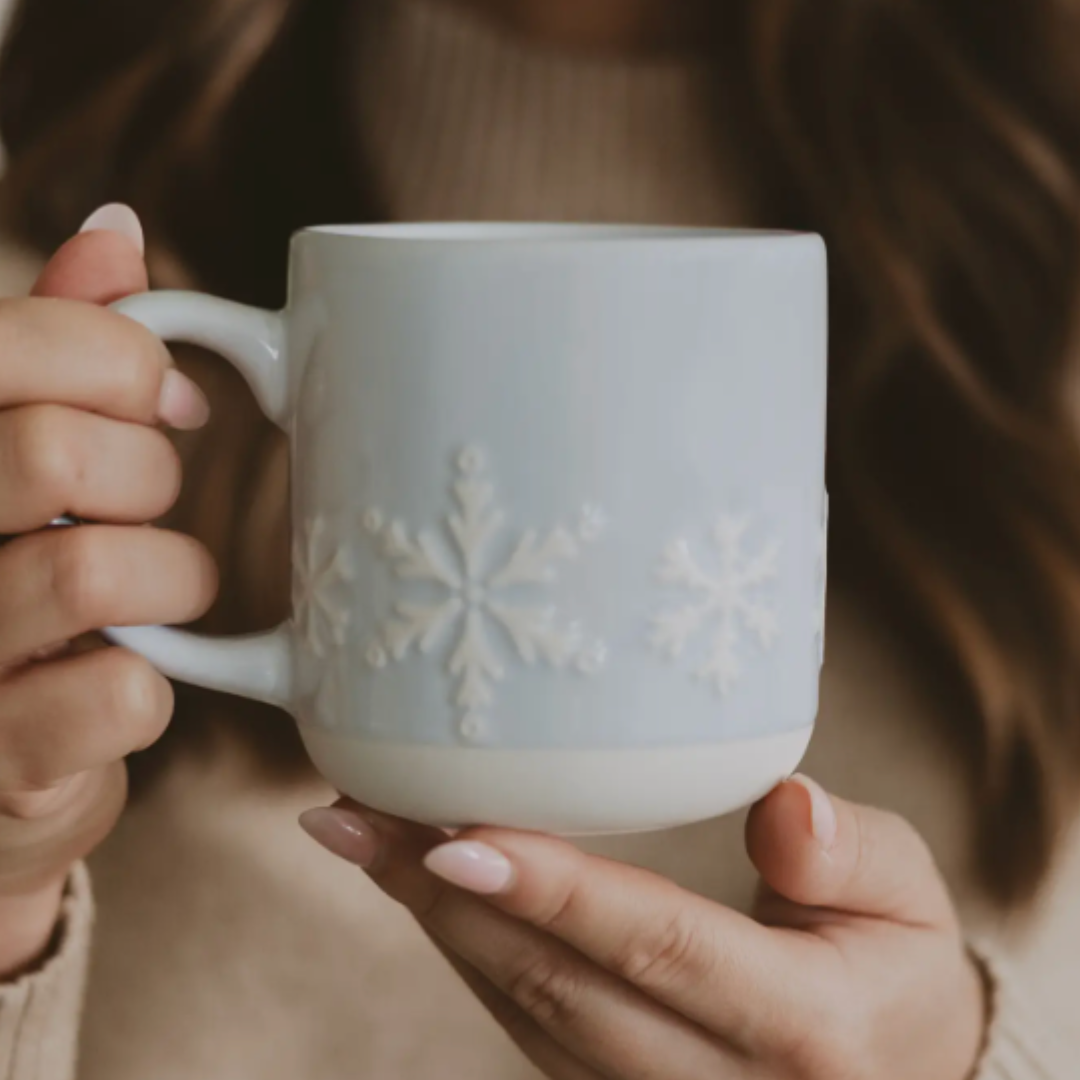 Person holding a light blue mug with white snowflake design.