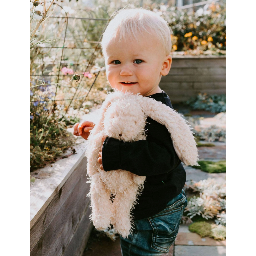 Child holding a fluffy bunny in a garden setting.