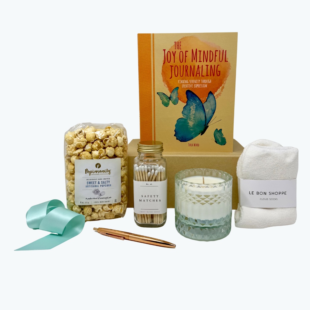 Gift box with popcorn, candle, matches, cozy socks, journal and pen on a white background.
