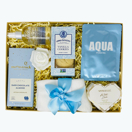 Gift set with products including a pillow spray, cookies, cozy socks, chocolate bar and skincare items in a decorative box.