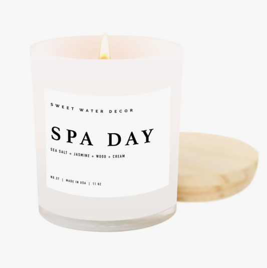 'Spa Day' Soy Candle: A white glass jar candle with a wooden lid, offering a tranquil ambiance for self-care rituals. This 11oz candle features a soothing blend of sea salt, jasmine, woody, and creamy notes, with a burn time of over 50 hours. Crafted with a cotton wick and soy-based wax, it's vegan, non-GMO, and free from phthalates and toxins.