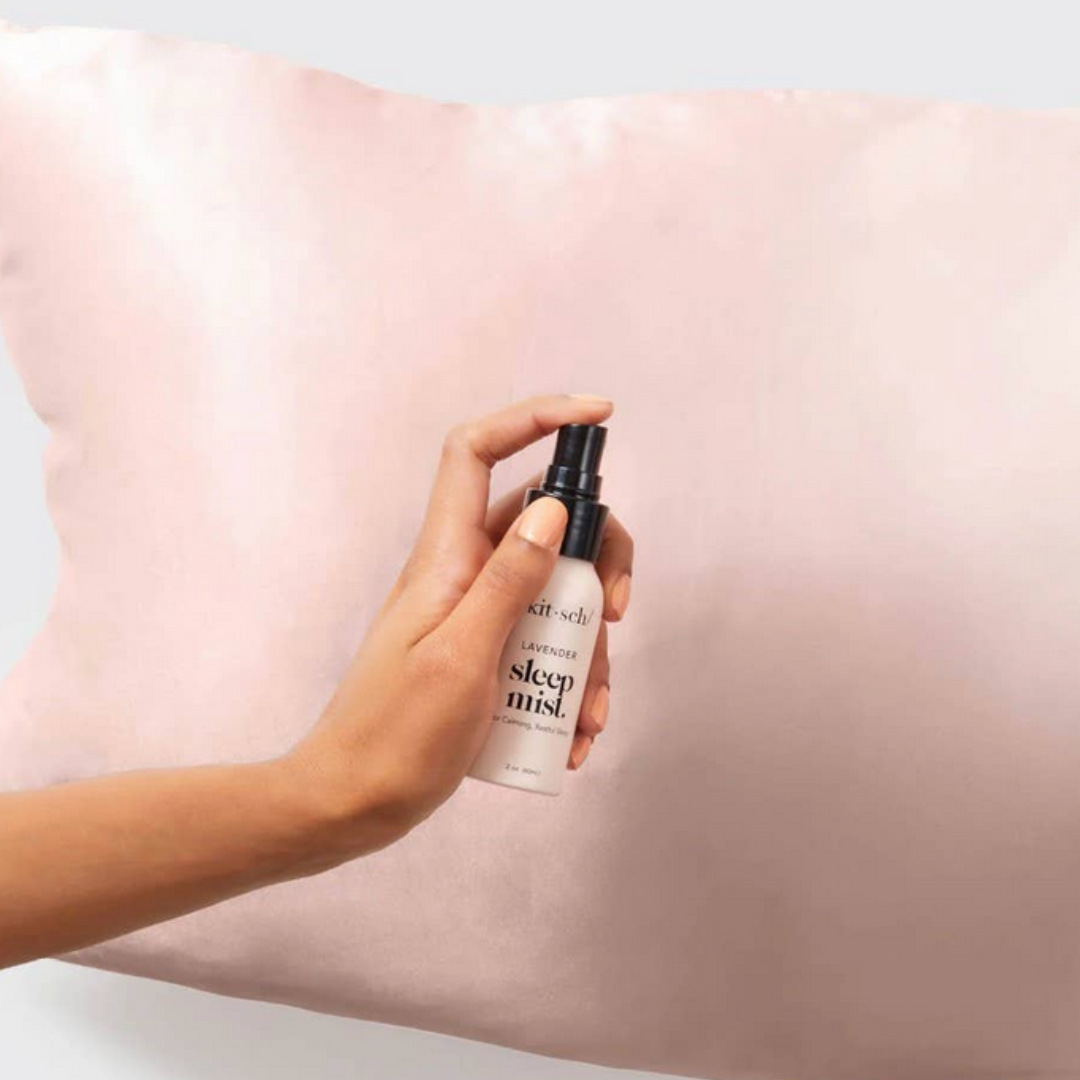 Hand holding a bottle of 'sleep mist' over a pink pillow.