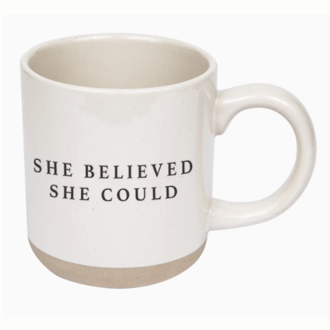 A cream-colored stoneware mug with a speckled finish, featuring the empowering phrase "She Believed She Could" in black lettering on both sides. The mug has a natural bottom and a unique hand-crafted look, suitable for coffee, tea, or hot chocolate. It’s microwave and dishwasher safe for convenience.