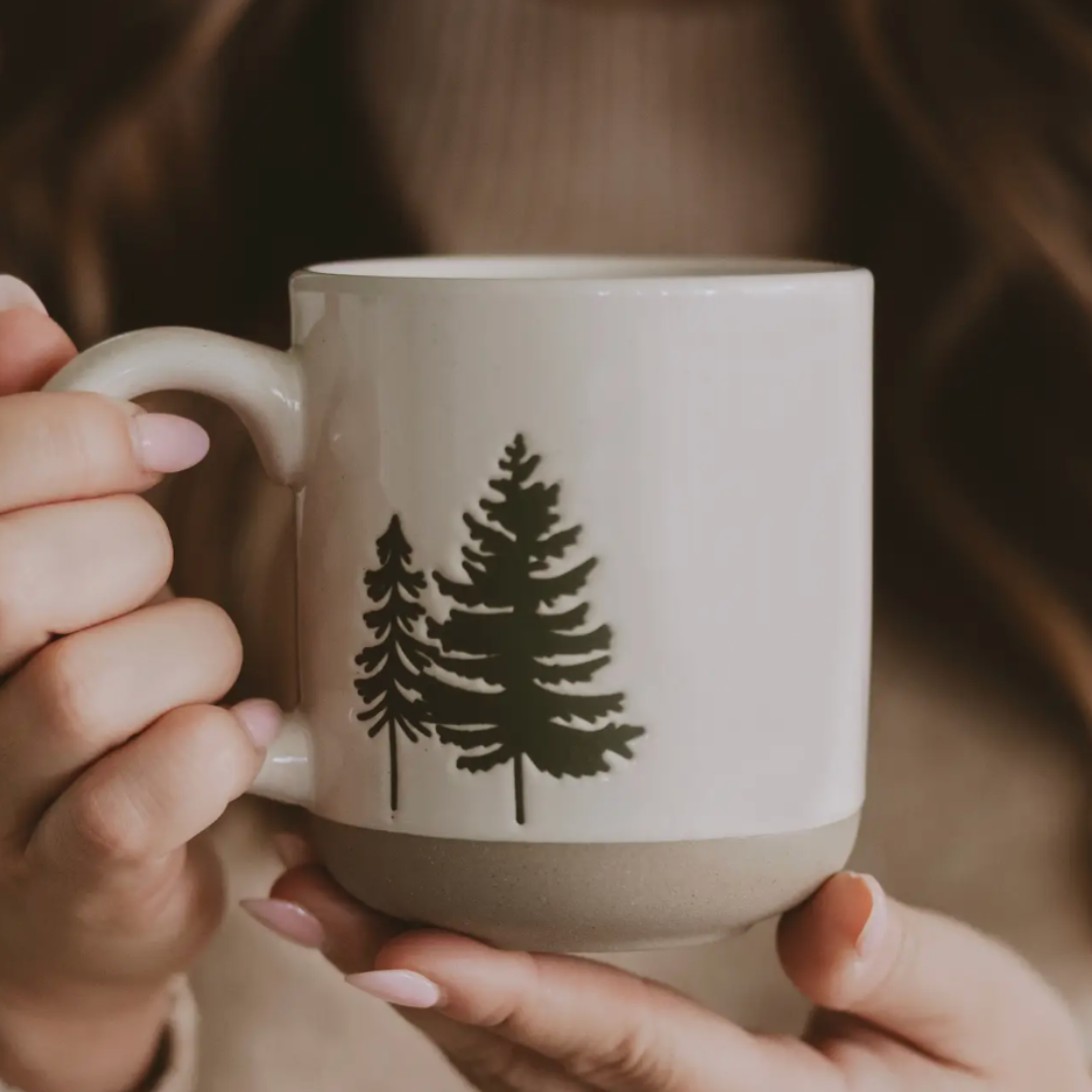 Person holding a mug with a tree design on a blurred background.