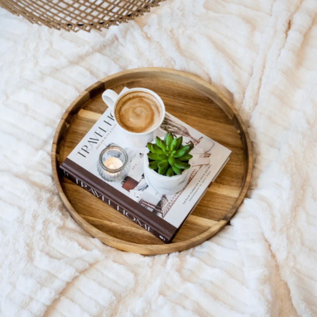 Wooden tray with a cup of coffee, book, and small plant on a textured white balnket.