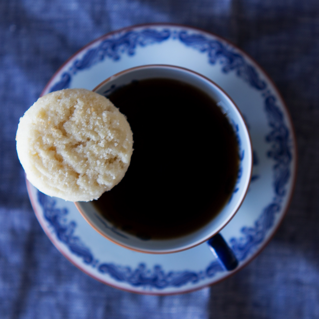 Cup of coffee with a vanilla Unna cookie on a blue and white tea cup and saucer.