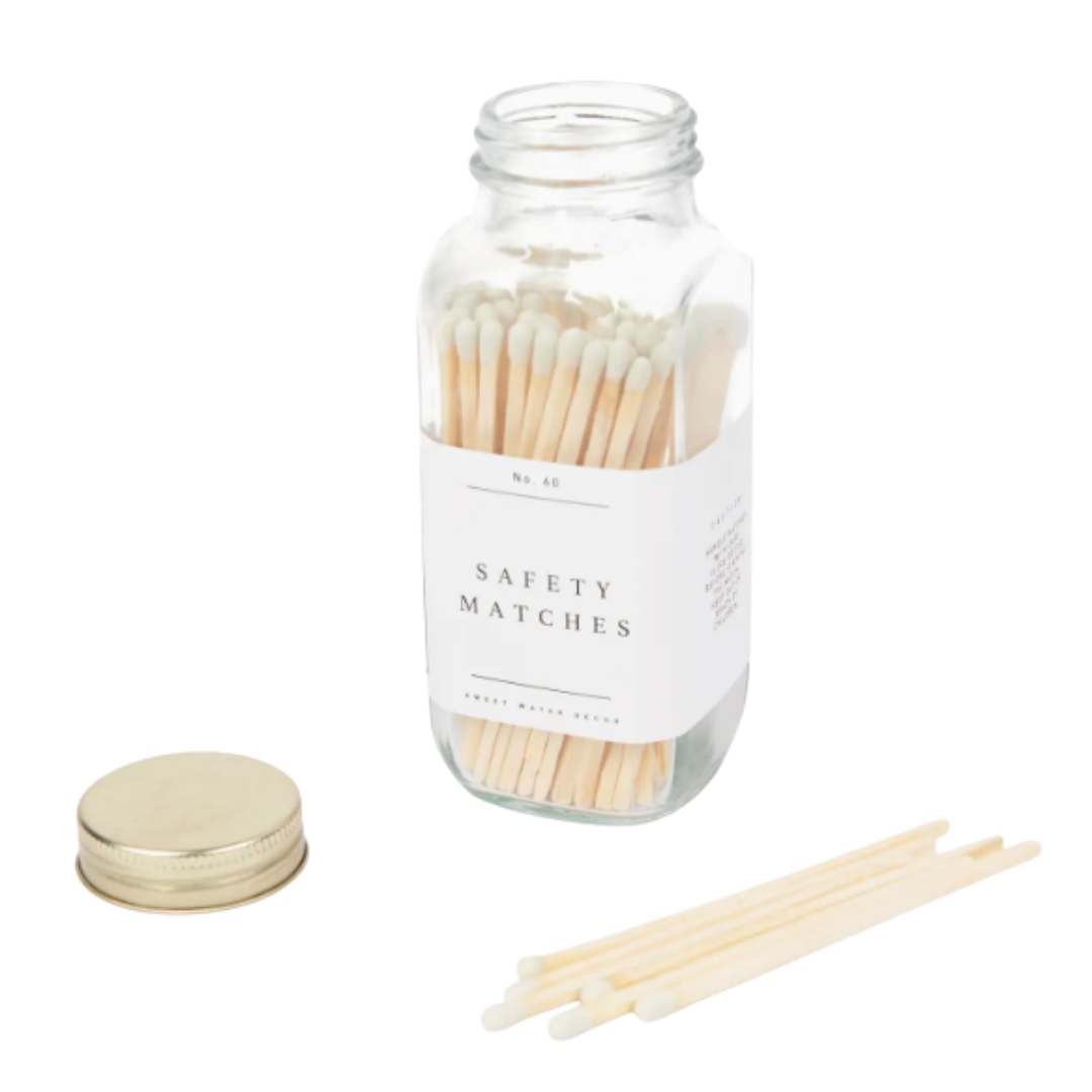 White tipped wooden Matches In Glass Bottle With Gold Lid. The gold lid is set next to the bottle with some matches as well set against a white background.