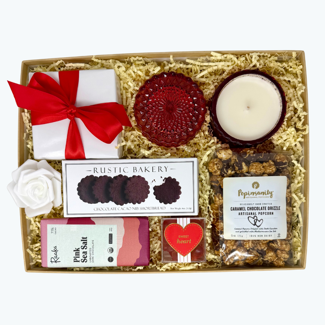 Gift box with assorted items including a candle, cookies, chocolate bar, and popcorn on a white background.