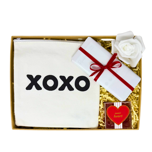 Gift set with a pouch, heart gummies, and chocolate in a box with a white rose and red ribbon.