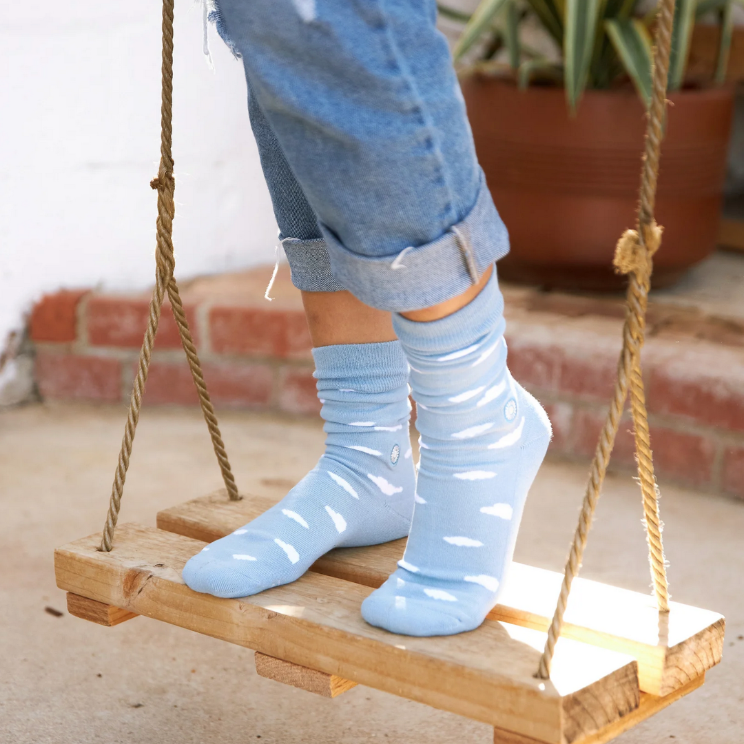 Person wearing light blue socks on a wooden swing with a blurred indoor background