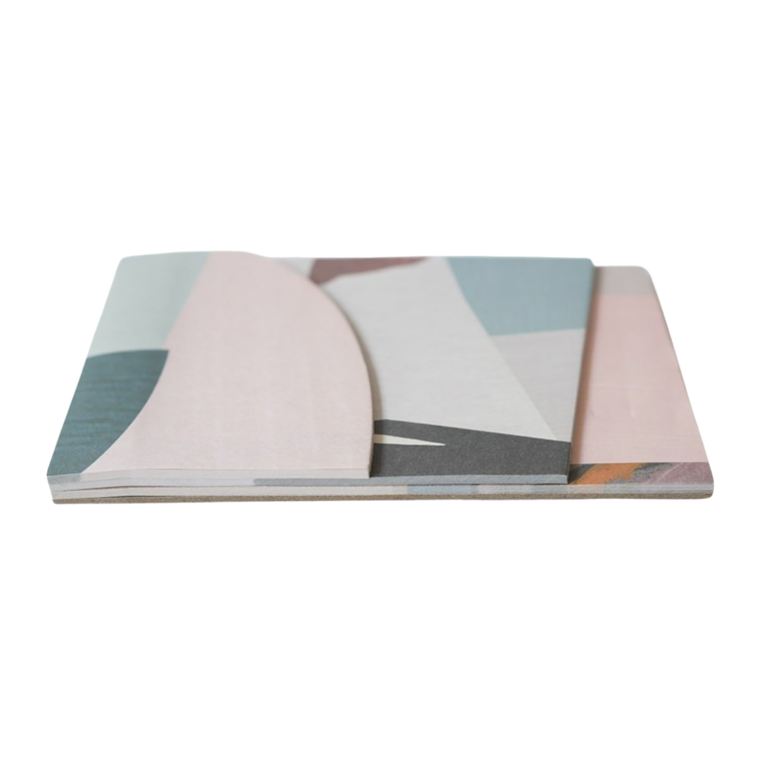 A stack of rectangular notebooks or journals with an abstract geometric pattern in pastel pink, blue, gray, and white, shown on a plain white background.