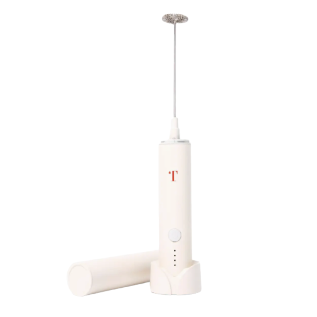 A white handheld electric frother with a matching white cylindrical attachment resting beside it, shown on a plain white background. The main body has a small red letter 'T' logo and a silver metal whisking head at the top.
